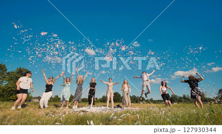 Group of joyful high school students throwing confetti in a summer field, celebrating graduation or end of school year 127930344