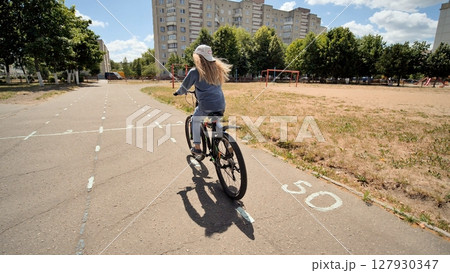 Young student pedaling bicycle through urban green space, sunlight illuminating surroundings Young student pedaling bicycle through urban green space, sunlight illuminating surroundings 127930347