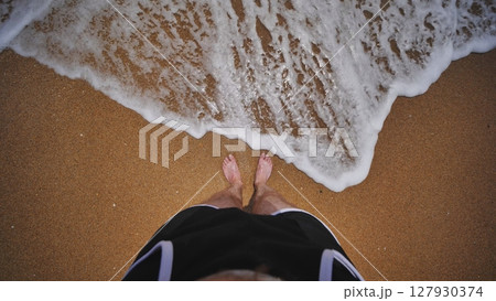 Tourist standing on Crimean beach enjoying foamy wave washing his feet Tourist standing on Crimean beach enjoying foamy wave washing his feet 127930374