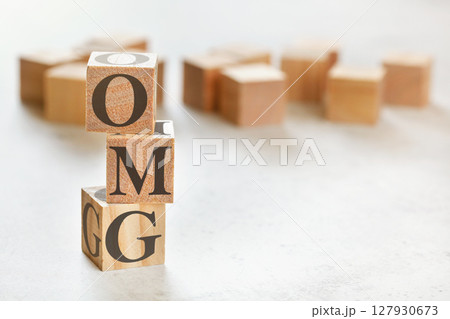 Three wooden cubes with letters OMG (short for Oh my God), on white table, more in background, space for text in right down corner Three wooden cubes with letters OMG (short for Oh my God), on white table, more in background, space for text in right down corner 127930673