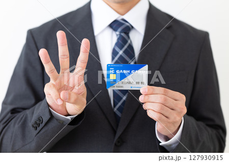 銀行のICキャッシュカードを持って3本指を立てるスーツを着たミドル男性ビジネスマン 127930915