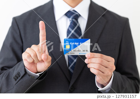 銀行のICキャッシュカードを持って人差し指を立てるスーツを着たミドル男性ビジネスマン 127931157
