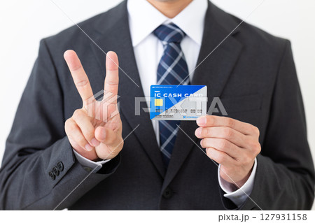 銀行のICキャッシュカードを持って2本指を立てるスーツを着たミドル男性ビジネスマン 127931158