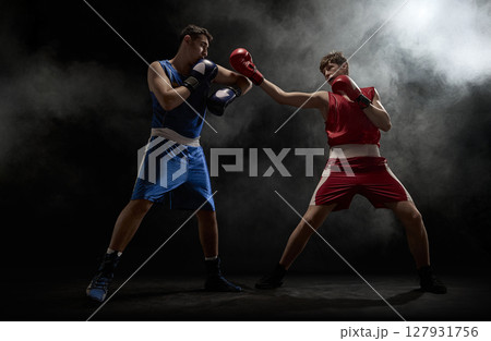 Two boxers engaged in intense match surrounded by dramatic smoke in dimly lit boxing ring 127931756