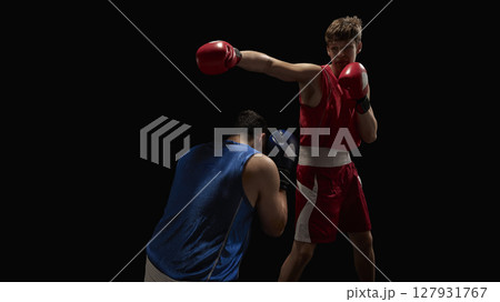 Boxer in red delivering punch to opponent in blue during intense match on dark background 127931767