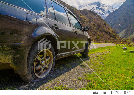 Car with flat tire parked in serene mountainous Kyrgyzstan region 127931874