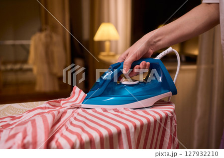 A person meticulously ironing clothes at home, ensuring all garments are neat and well cared for 127932210