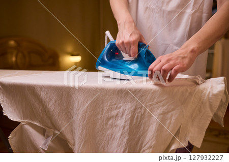 A person meticulously ironing clothes at home, ensuring all garments are neat and well cared for A person meticulously ironing clothes at home, ensuring all garments are neat and well cared for 127932227