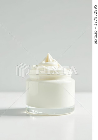 White cream swirling in a glass jar on white surface with vertical composition 127932995