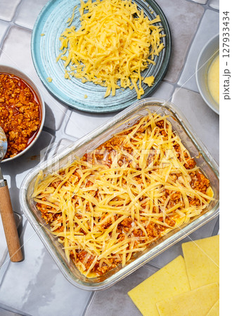 Lasagna Preparation with Meat Sauce and Grated Cheese in Glass Baking Dish. Cooking Italian Pasta for Dinner. Lasagna Preparation with Meat Sauce and Grated Cheese in Glass Baking Dish. Cooking Italian Pasta for Dinner. 127933434