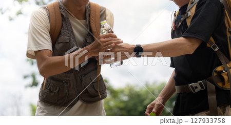 Father and Son Sharing Water on Hike. A father hands a water bottle to his son during their outdoor adventure. Father and Son Sharing Water on Hike. A father hands a water bottle to his son during their outdoor adventure. 127933758