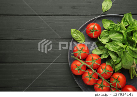 Cherry tomatoes and green basil on dark plate on black background 127934145