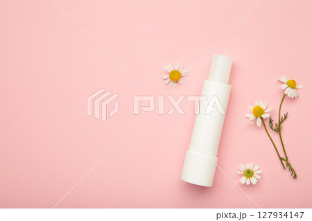 Lip balms and chamomile flowers on pink background. 127934147