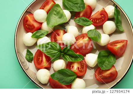 Italian Caprese salad with cherry tomatoes, mozzarella, basil on plate on mint background. Italian Caprese salad with cherry tomatoes, mozzarella, basil on plate on mint background. 127934174