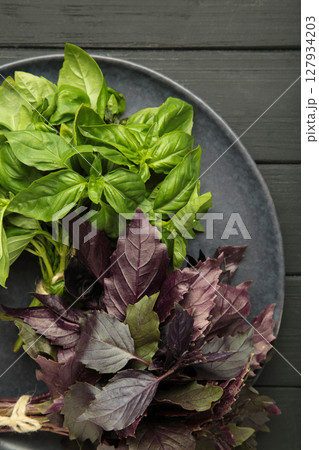 Green and purple basil herb on dark plate on black background. Vertical photo 127934203