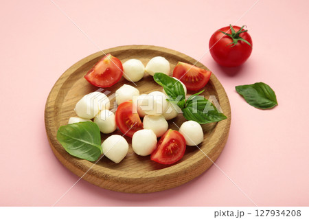 Italian Caprese salad with cherry tomatoes, mozzarella, basil on wooden plate on pink background. Italian Caprese salad with cherry tomatoes, mozzarella, basil on wooden plate on pink background. 127934208