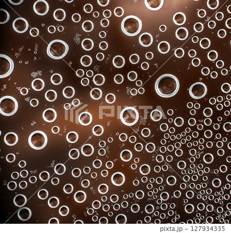 Close-up of carbonated bubbles rising in a fizzy brown beverage, creating a dynamic abstract pattern of circular shapes and light reflections 127934335