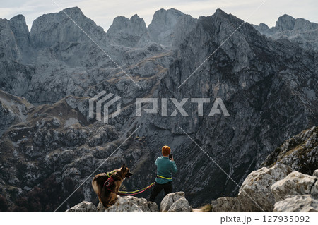 A woman photographing or making video of rugged mountains of Prokletije in Montenegro with her German and Australian Shepherd by her side, enjoying the beauty of the autumn wilderness 127935092