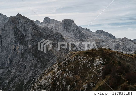 Steep rocky peaks of Prokletije mountains tower above grassy ridges in Montenegro under a cloudy autumn sky 127935191