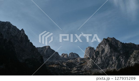 Panoramic view of jagged limestone peaks in Prokletije Mountains under soft morning light and dramatic blue sky. Nature of Montenegro country 127935209