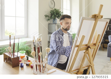 An artist paints in a bright studio filled with colorful supplies and materials 127935315