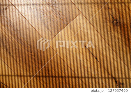 Light and shadows create patterns on wooden flooring in a sunlit room during a quiet afternoon 127937490