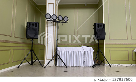 Sound system with large speakers and stage lighting setup in an elegant event hall. Scene is prepared for corporate event, wedding, or celebration, emphasizing professional audio visual equipment 127937600