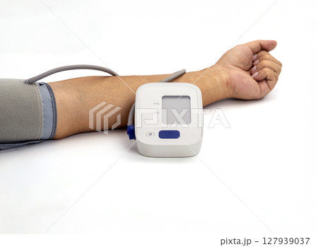 Digital blood pressure monitor is wrapped around arm, displaying modern medical device used for measuring blood pressure. setup is on clean, white background, emphasizing equipment functionality 127939037