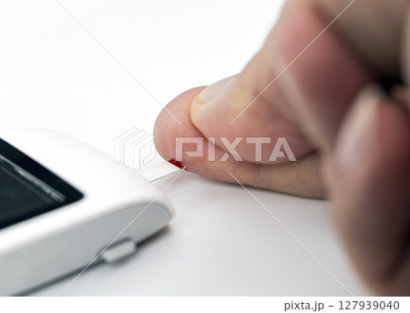 Person using blood glucose test device to check their blood sugar level by pricking their finger. image focuses on hand and device, highlighting process of monitoring diabetes 127939040