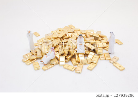 Miniature Figures Standing Around Pile of Shiny Gold Bars 127939286