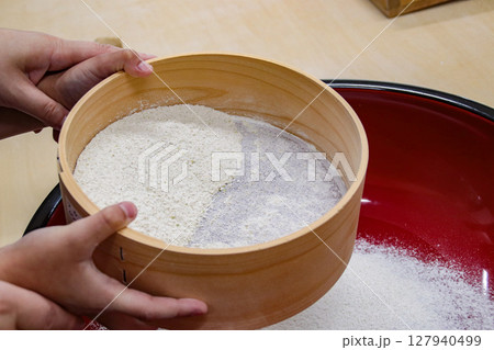 大人と一緒に蕎麦粉をふるいにかける子供(7歳児/男の子) 大人と一緒に蕎麦粉をふるいにかける子供(7歳児/男の子) 127940499