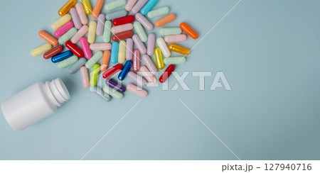 Top view white bottle container with many medication capsules on blue background with copy space. 127940716