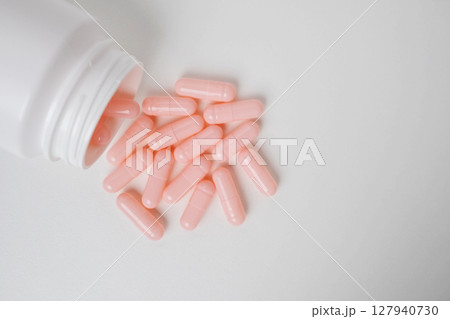 Top view bottle container with pink medication capsules on white background with copy space. Top view bottle container with pink medication capsules on white background with copy space. 127940730