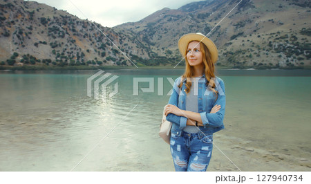 Happy young woman tourist standing on lake with mountains background. Greece, island Crete 127940734