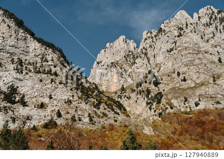 Sharp ridges and colorful forested slopes of the Prokletije mountains in autumn, captured in warm light under a clear blue sky. Nature of Montenegro 127940889