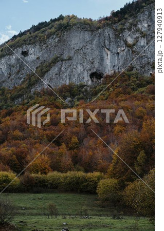 Towering cliffs with caves rise above a vibrant forest in autumn colors in Prokletije National Park, Montenegro country 127940913