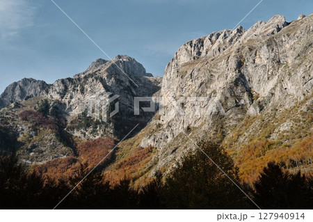 Sharp ridges and colorful forested slopes of the Prokletije mountains in autumn, captured in warm light under a clear blue sky. Nature of Montenegro 127940914