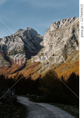 Narrow trail winding through vibrant autumn forest beneath steep cliffs in Prokletije National Park, Montenegro, a peaceful hiking scene 127940915