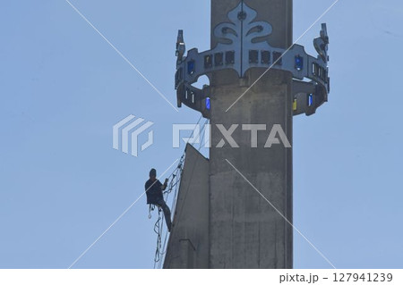 A skilled worker fixes the tower of a modern church. A roofer works on the tower of a modern building. The concept of working at height and safety at work A skilled worker fixes the tower of a modern church. A roofer works on the tower of a modern building. The concept of working at height and safety at work 127941239