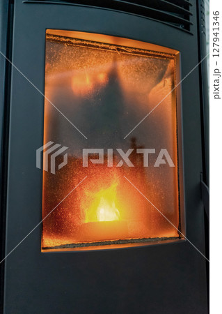 Vertical shot of a modern pellet stove in full operation with a large flame and a very dirty door window. Renewable and sustainable energy, ecological heat. 127941346