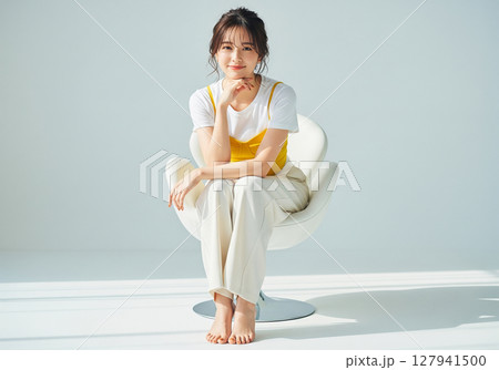 白い背景の白い椅子に座る、白Tシャツと黄色キャミソールの女性モデル 白い背景の白い椅子に座る、白Tシャツと黄色キャミソールの女性モデル 127941500