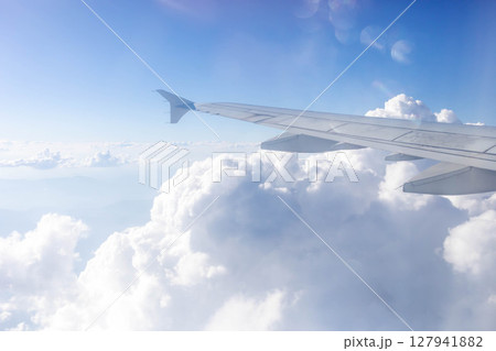 Airplane wing above fluffy white clouds with bright blue sky and sunlight shining through Airplane wing above fluffy white clouds with bright blue sky and sunlight shining through 127941882