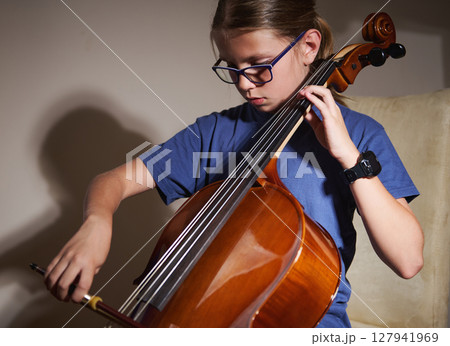 Young Girl Practicing the Cello with Focus and Passion in Natural Lighting 127941969