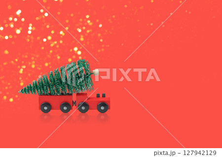 Winter fairy tale composition of green Christmas trees and red steam train carrying Christmas tree on red background. Concept of Christmas, holiday, congratulations 127942129
