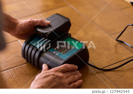 A handyman is actively installing various equipment using a powerful drill on a wooden floor 127942545