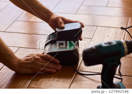 A handyman is actively installing various equipment using a powerful drill on a wooden floor 127942546