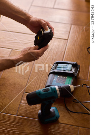 A handyman is actively installing various equipment using a powerful drill on a wooden floor 127942548