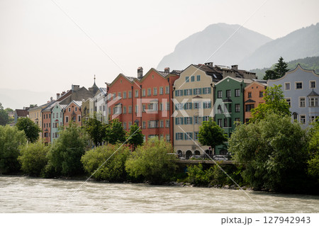 Colorful historic houses along Inn River in Innsbruck, Austria with mountain backdrop 127942943