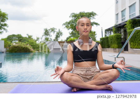 Non-binary person exercising in poolside doing yoga and wearing sport bra 127942978