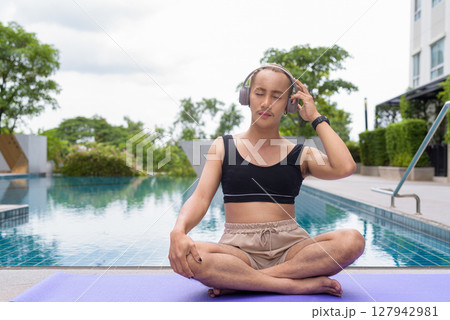 Non-binary person exercising in poolside doing yoga and wearing sport bra 127942981
